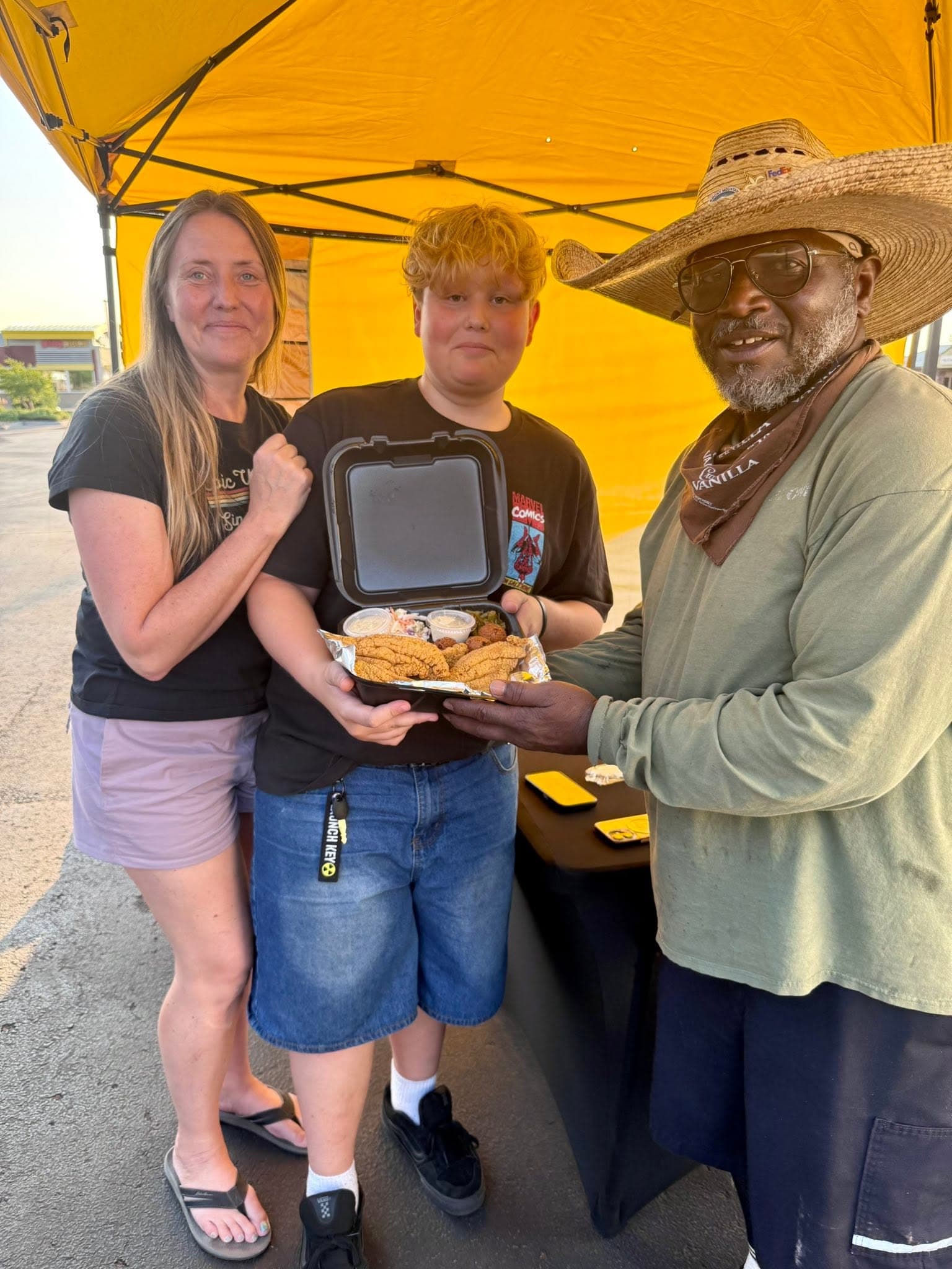 Three team members under a yellow tent with fried food